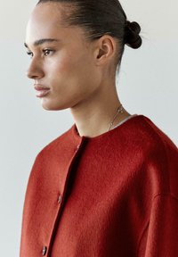 Cardigan in lana rossa con scollo arrotondato e chiusura con bottoni, caratterizzato da un tessuto a maglia testurizzato e un design semplice.