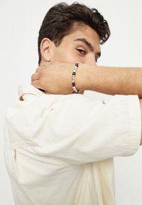 Pulsera de cuentas con cuentas alternas de metal plateado y madera oscura, mostrada en una muñeca con una camisa de color claro de fondo.