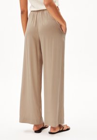 Béžové široké kalhoty vyrobené z hladké látky, s elastickým pasem, bočními kapsami a splývavým siluetou.