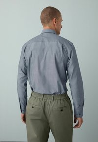 Graues langärmliges Hemd mit Button-Down-Kragen, kombiniert mit hellgrünen Hosen mit elastischem Bund. Mit Rückenschulter und geknöpften Manschetten.