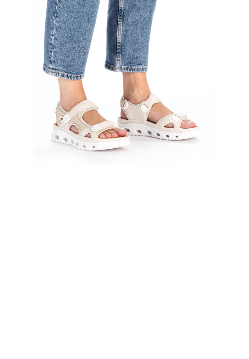 Light beige sandals with open toe and side cutouts. Features adjustable straps and a thick white sole with ventilation holes.