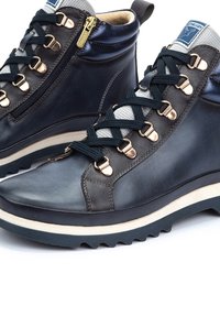 Bottes montantes en cuir bleu marine avec une fermeture éclair sur le côté, des accents métalliques, un tissu texturé gris et une épaisse semelle blanche avec un motif cranté.