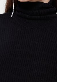 Černý žebrovaný rolák s přiléhavým střihem a strukturovanou tkaninou, s vysokým límcem a jemným leskem materiálu.