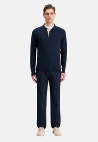 Polo de manga larga azul marino con cuello beige, combinado con pantalones azul marino con pliegues y zapatillas de colores claros. Diseño simple y moderno.