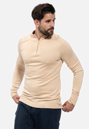Jersey beige de manga larga con cuello de cremallera de un cuarto. Presenta puños y dobladillo acanalados, hecho de una tela suave con una textura lisa.