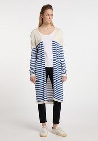 Dlouhý cardigan s modro-bílými pruhy, otevřeným předním designem a dlouhými rukávy. Nnošený přes bílý top a černé kalhoty. Strukturovaná pletená tkanina.