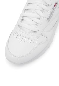 Balti odiniai sportbačiai su perforuota pirštų danga, plokščiais raišteliais ir dekoratyvinėmis siūlėmis. Yra Reebok logotipas su Jungtinės Karalystės vėliavos akcentu.