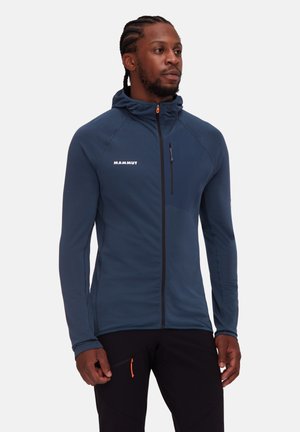 Veste bleu marine avec zip devant, capuche et accents noirs. Caractéristiques d'un tissu texturé, logo de la marque et poche poitrine zippée.