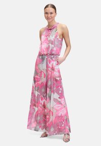 Combinaison longue à fleurs dans des tons roses et gris, dotée d'un design sans manches, d'une taille élastique et de poches latérales. Confectionnée en tissu léger.