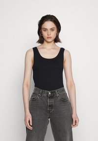 Top de alças preto com decote em U, feito de um tecido suave, combinado com jeans cinzentos desbotados de cintura alta, com costuras e bolsos visíveis.