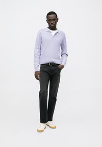 Polo de punto color lila claro, vaqueros negros y zapatillas crema. Corte ajustado, tela texturizada, con cuello y mangas largas.