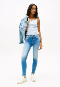 Top de tirantes de color azul claro con ribetes de encaje, combinado con jeans ajustados de color azul desgastado y zapatillas blancas. Chaqueta de mezclilla colgada del hombro.