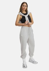 Grijze katoenen joggers met elastische boorden, een bijpassende grijze sweatshirt die op de schouders is geknoopt en een zwarte cropped top; gedragen met grijze sneakers.