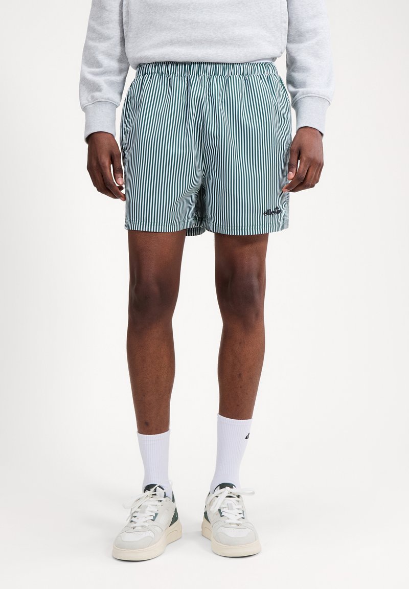 Άνδρας που φοράει πράσινα και λευκά κάθετα ριγέ σορτς, λευκές κάλτσες μέχρι τον αστράγαλο, λευκά αθλητικά παπούτσια και ανοιχτό γκρι φούτερ.