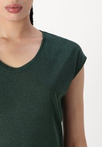 Green short-sleeve top made from textured fabric, featuring a v-neckline and rolled sleeves. Material has a slight shimmer.