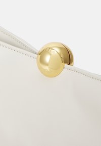 Borsa in pelle bianca con una chiusura rotonda in tono oro con marchio in rilievo. Testura liscia e design minimalista con linee pulite.