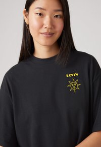 Black cotton t-shirt featuring yellow "Levi's" text and a sun graphic on the left chest. Short sleeves and a relaxed fit.