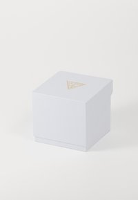 Balta tekstūruota dėžutė su auksiniu trikampiu logotipu viršuje, pasižyminti saugiu dangčiu ir kvadratine forma. Minimalistinis dizainas ir lygus paviršius.