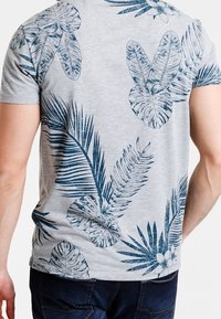 Kortærmet grå t-shirt med et blåt tropisk bladprint, med detaljerede blade og blomsteraccentueringer over ryggen.