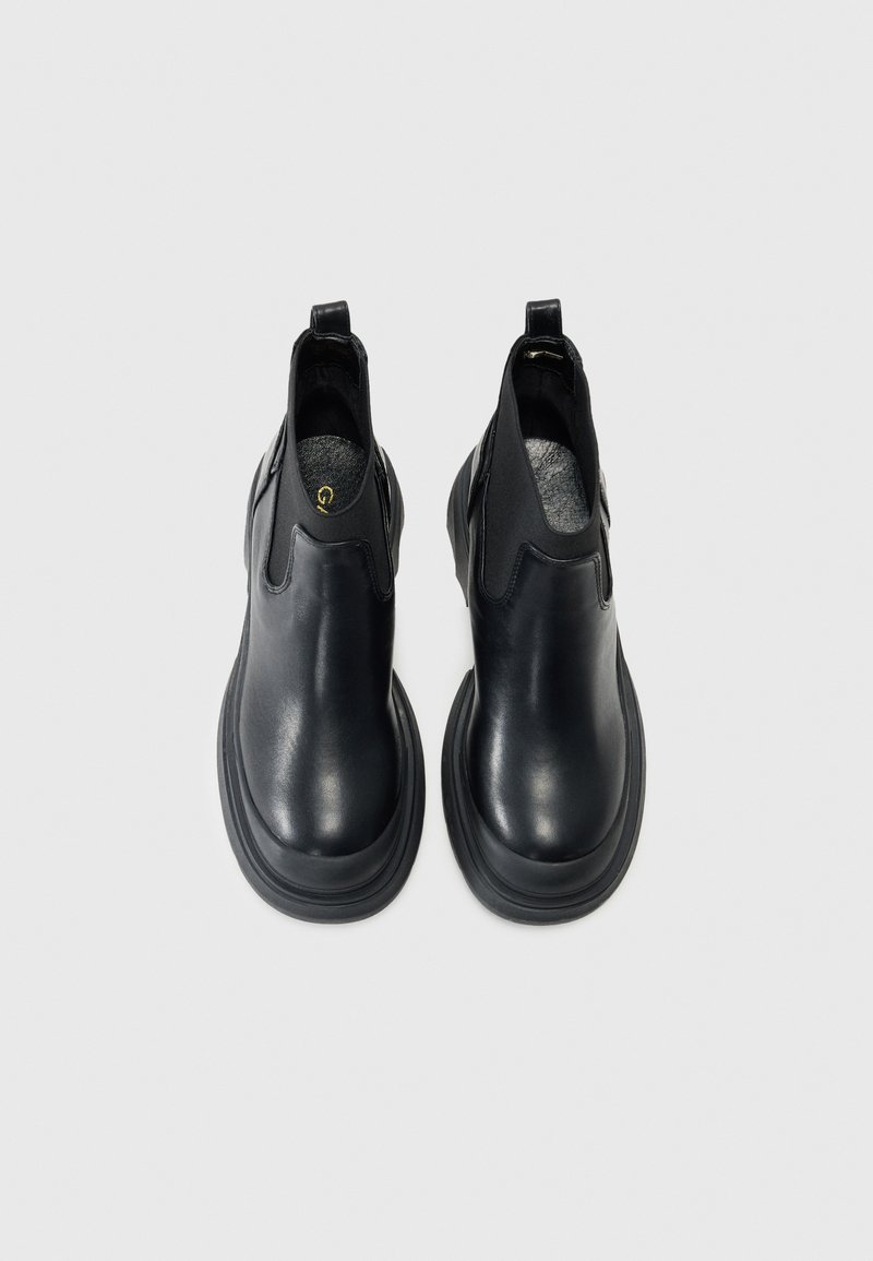 Bottines en cuir noir avec panneaux latéraux élastiques, bout rond et semelle en caoutchouc épaisse. Présente un petit tiret à l'arrière pour un enfilage facile.