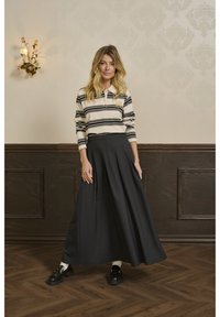 Stribet langærmet polo skjorte i crème og sort, parret med en mørk, flydende maxi-nederdel. Sorte loafers med kraftige såler fuldender outfittet.
