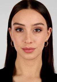 Orecchini a cerchio in oro con superficie texturizzata e piccoli accenti simili a diamanti, indossati da una persona con capelli lunghi e lisci di colore scuro e trucco naturale.