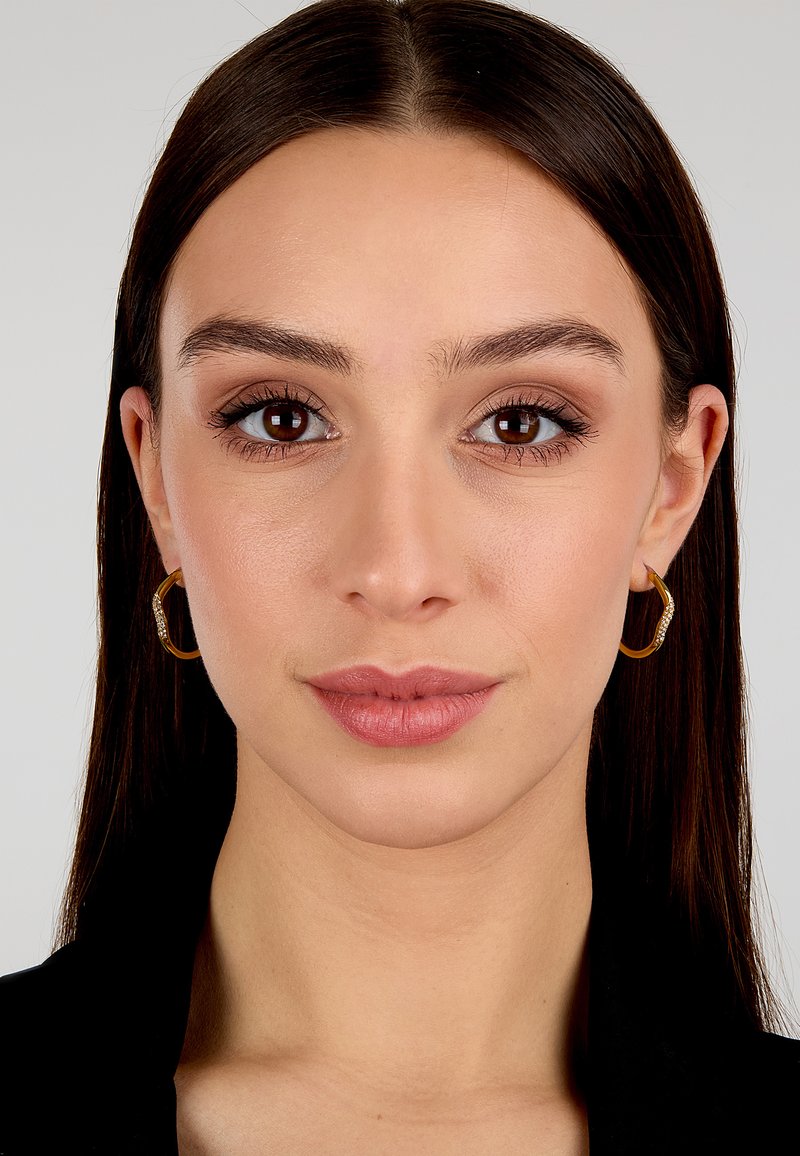 Orecchini a cerchio in oro con superficie texturizzata e piccoli accenti simili a diamanti, indossati da una persona con capelli lunghi e lisci di colore scuro e trucco naturale.