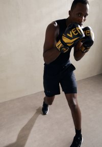 Black boxing gloves with yellow accents, fitted black tank top, and black shorts. The figure is in a fighting stance on a light gray surface.