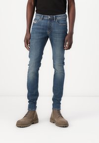 Tettsynte blå denimjeans med middels vask, femlommers design og lett slitasje. Kombinert med brune snøringstøvler.