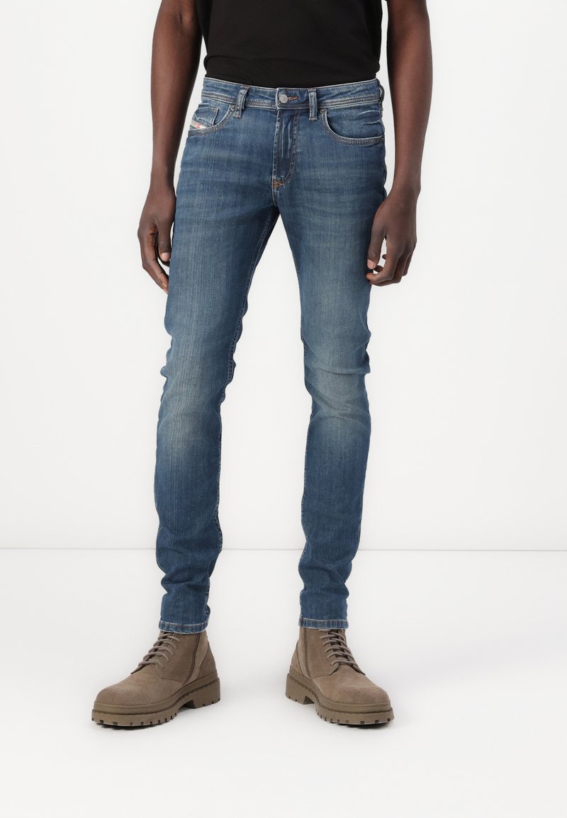 Tettsynte blå denimjeans med middels vask, femlommers design og lett slitasje. Kombinert med brune snøringstøvler.
