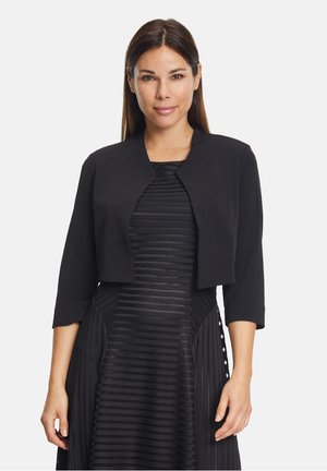 Rövidített fekete dzseki háromnegyedes ujjakkal, sima anyagból készült. Kerek nyakú, minimalista dizájnja van, pleats dresszel párosítható.
