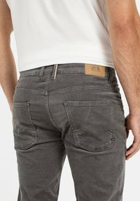 Grijze corduroy broek met een gestructureerde afwerking, voorzien van twee achterzakken en een tan leren merklabel op de tailleband.