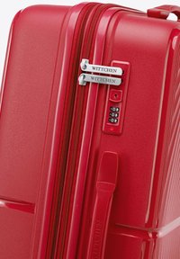 Valigia rigida rossa con superficie texturizzata, doppie cerniere e lucchetto a combinazione. Presenta marchio e bordi lisci.