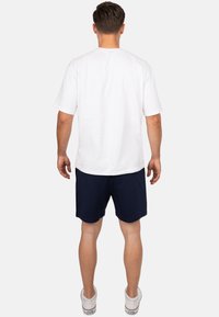 T-shirt bianco a maniche corte, in misto cotone, taglio rilassato. Abbinato a pantaloni corti blu navy, con texture liscia, cintura elastica e sneakers bianche.