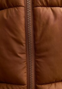 Brązowa wyściełana tkanina z centralnym zamkiem błyskawicznym wyposażonym w ząbki z tworzywa sztucznego zazębiające się oraz szczegółowe przeszycia po obu stronach.