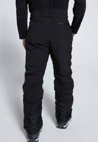 Schwarze wasserdichte Skihosen mit hohem Bund, tapered Beinen und einer Reißverschlusstasche auf der Rückseite, charakterisiert durch eine glatte Textur und ein einfaches Design.