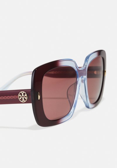 Ochelari de soare supradimensionați cu rame cărămizii și bleu deschis, lentile cu degradé și accesorii aurii cu un logo pe brațe.