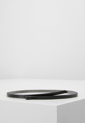 Ceinture fine en cuir noir enroulée sur une surface blanche sur fond gris clair uni.