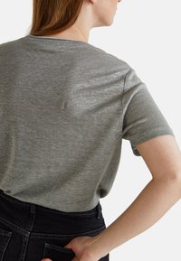 T-shirt gris à manches courtes avec une texture douce et un léger brillant, présentant une coupe décontractée et un subtil détail de couture le long de l'encolure.