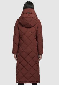 Lang, quilted pufferjakke i dyb rød med en stor, justerbar hætte. Har skrå syninger og sidelommer med lynlås for nem påklædning.