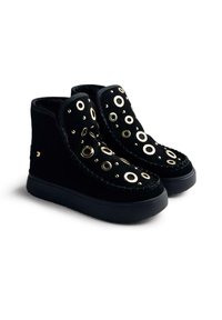 Botines de ante negro con ojales circulares dorados, costuras decorativas y suela de goma negra contrastante. Diseño clásico con acentos únicos.