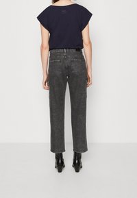 Dunkelgraue Denim-Jeans mit lockerer Passform und geradem Bein, ausgestattet mit Gesäßtaschen und dezenter Stickerei, kombiniert mit einem schwarzen, cropped T-Shirt.