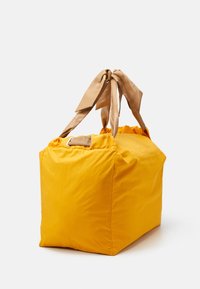 Żółta torba z materiału o prostokątnym kształcie, z beżowymi wstążkami w formie kokardek i marszczoną górą. Gładka, lekka tekstura.