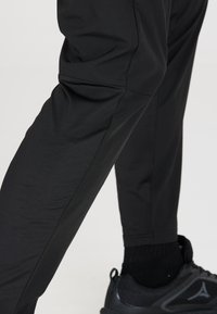 Zwarte sportbroek gemaakt van lichtgewicht, gestructureerde stof met een slim fit en subtiele naden, gecombineerd met zwarte sportschoenen.