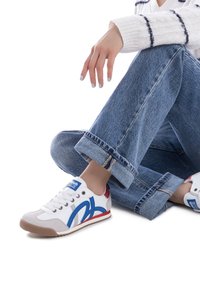 Zapatilla blanca con acentos en azul y rojo, suela de goma y diseño con cordones. Combinada con unos jeans de tiro bajo en azul claro arremangados.