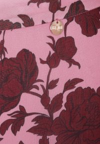 Bloemstoffen in roze met een donker bordeauxrood rozen- en bladerenpatroon. Bevat een kleine gouden merkknop op de naad.