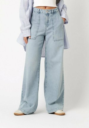 Person wearing light blue wide-leg jeans with large front pockets, white crop top, striped long shirt, and white shoes.