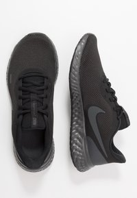 Des chaussures de course Nike noires avec des semelles texturées, des tiges en mesh et des lacets, présentées de dessus et sur le côté sur un fond blanc.