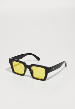 Ochelari de soare pătrați cu ramă mată neagră și lentile galbene. Prezintă un design geometric și un logo subtil pe lateral.