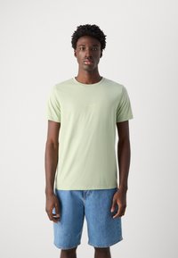 Lys grønne bomull T-skjorte med rund hals, korte ermer, og en liten "Ciao Bella" tekstlogo i gull i midten. Kombinert med denim shorts.